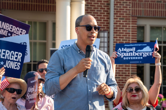 Jay Jones speaks holding a microphone outside in front of people holding signs that say "Abigail Spanberger Governor"