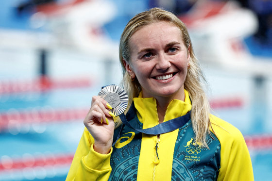 Ariarne Titmus smiles while holding onto a silver medal that she's wearing around her neck