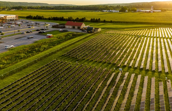 Sunset beams reflect in solar farm panels in Pennsylvania rolling farmlands and commercial zone in Brodheadsville, Poconos.