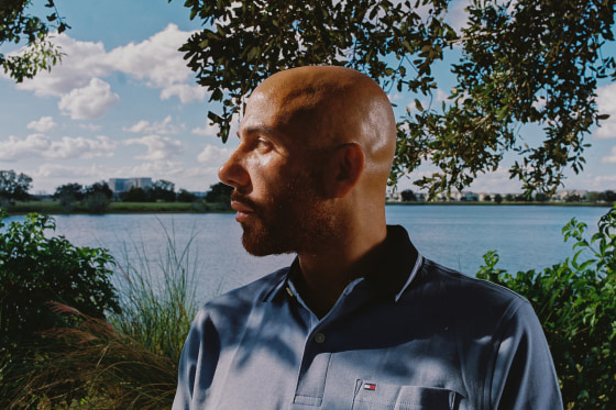Giuseppe Corletto looks to his right in front of a lake, trees, and tall grass