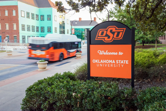 Oklahoma State University welcome sign seen outside next to a street with a bus passing by