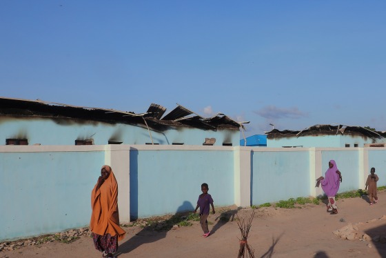 People walk past torched houses outside