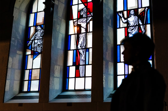 Pastor stands silhouetted by stained glass windows.