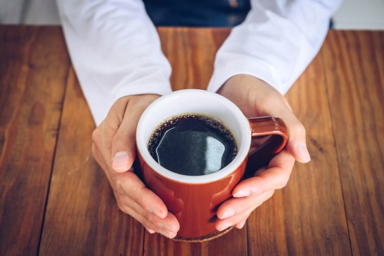 Hands holding a mug of black coffee