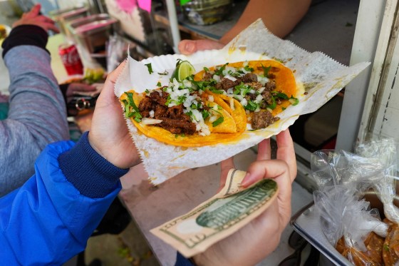 A hand exchanges a $10 bill for a plate of street tacos.