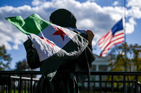 A man holds a Syrian flag across the street from the White House.