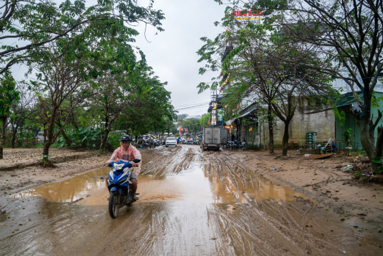 A person on a motorbike drives atop a muddy road over a puddle