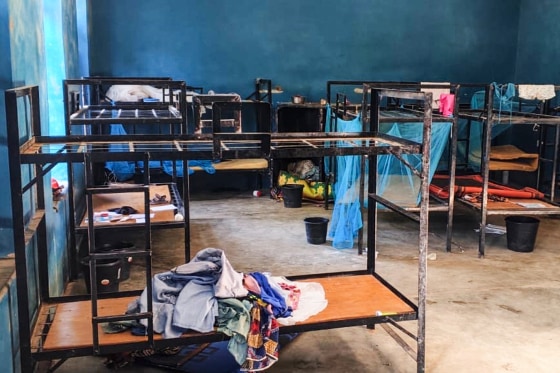 A room with bunkbeds that are stripped of mattresses, with clothes and blankets laying around