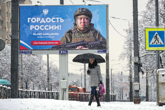 A person walks past a billboard showing a Russian soldier participating in military actions in the Ukraine reading: "The pride of Russia",