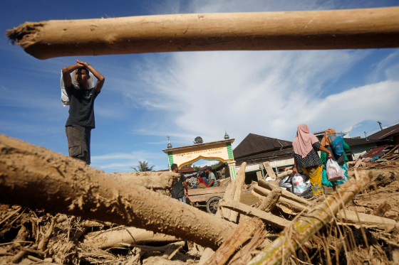 Survivors walk past logs swept away by a flash flood in Batang Toru, North Sumatra