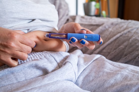 Unrecognizable mature overweight diabetic woman injecting a syringe of semaglutide into her stomach.