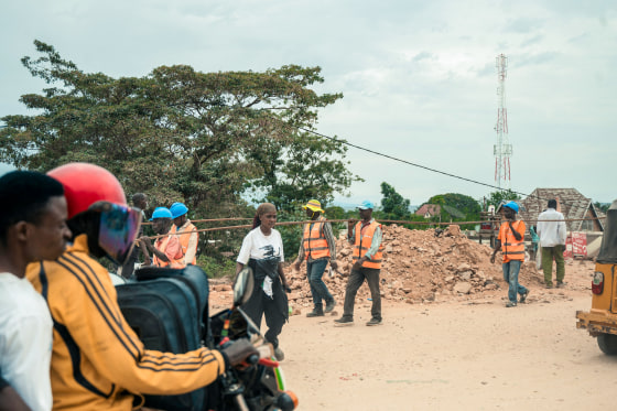 People walk and ride motorbikes along a dirt road