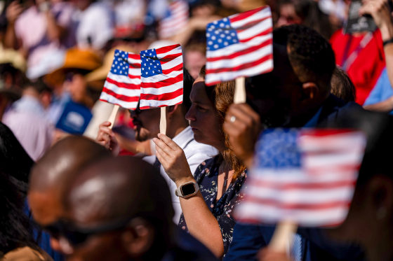 Images: New US citizens use handheld fans to take shade from the sun during a naturalization ceremony