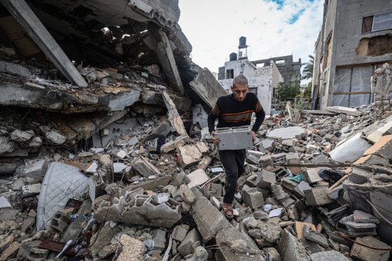 A person holds a cinderblock while walking on top of rubble outside