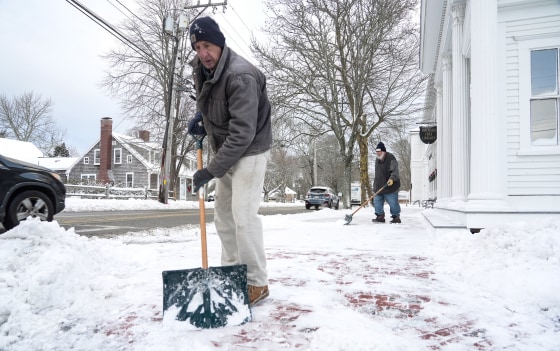 People shovel snow off of a sidewalk