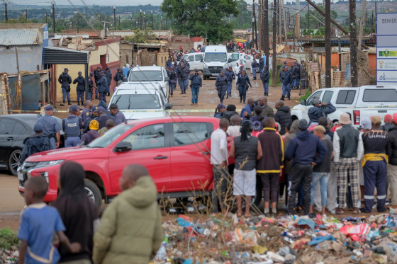 Residents wathch as South African Police Service (SAPS) officers gather at the scene of an attack at a tavern in Bekkersdal on Dec. 21