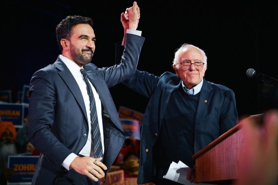 Zohran Mamdani, left, and Bernie Sanders stand together on stage and hold hands while raising them up