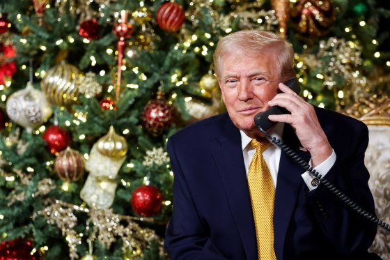Donald Trump holds a landline telephone while seated in front of a Christmas tree