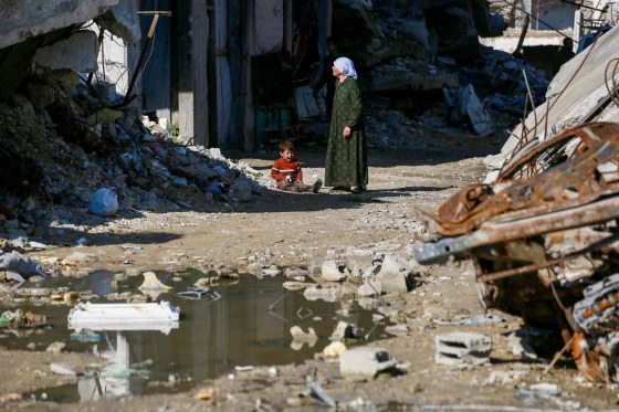 A Palestinian woman stands with a child next to the rubble of destroyed building.