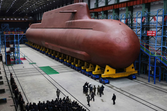 A large submarine is seen inside of a building as people look on