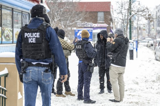 ICE agents question a man outside of a store on a sidewalk, it's snowing