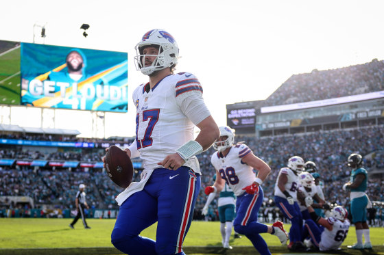 Josh Allen holds a football while walking on the football field in uniform