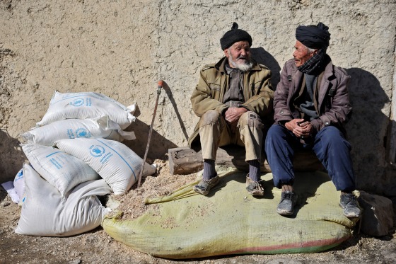 Afghan men sit next to sacks of flour outside