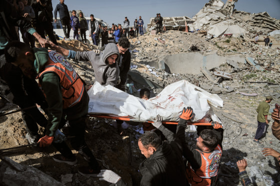 People carry a body wrapped in white tarp out from the rubble