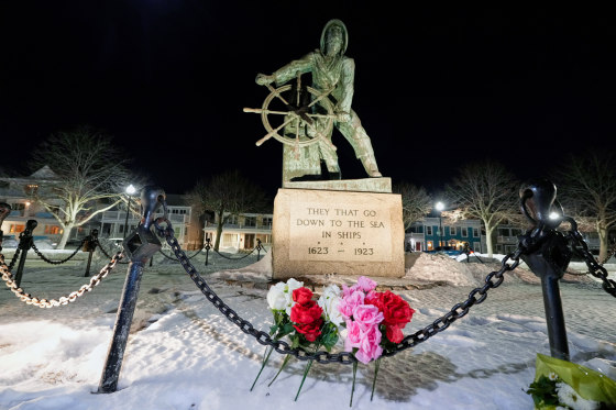 Flowers at the bottom of a memorial statue outside, the plaque on the statue reads "they that go down to the sea in ships"