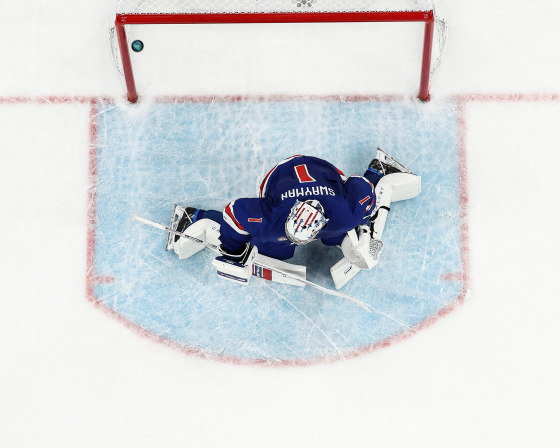 An overhead view of a goalie on the ice, in front of a puck that has drifted past the goal line and into the net.