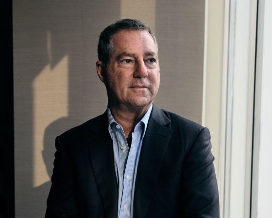 Brad Karp rests on a marble windowsill while posing for a portrait. He gazes off-camera to his left.