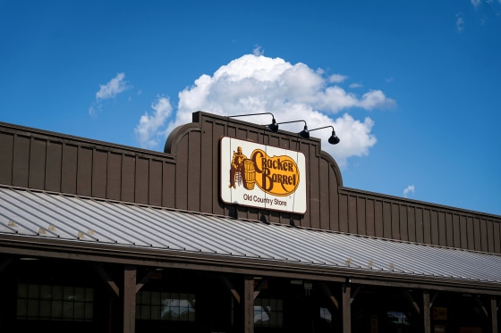 The orange and white Cracker Barrel logo is displayed on a brown building's facade, under clear blue skies.