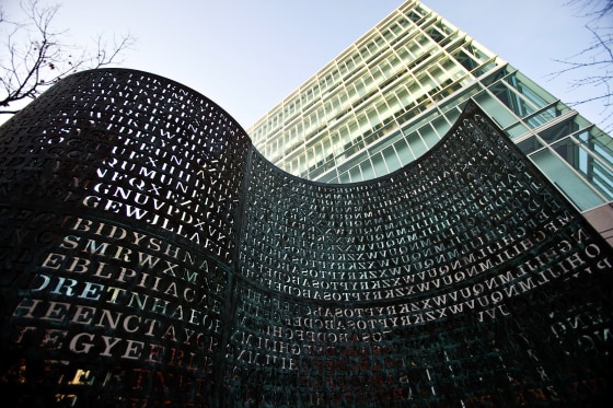 A sculpture with small lettering appears in the foreground of an image. The CIA headquarters rises above it in the background.
