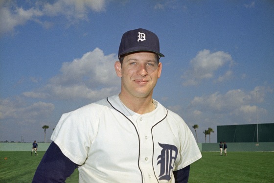 Mickey Lolich smiles while standing on a baseball field. He is wearing a white and navy blue uniform.