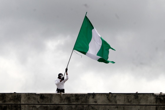 A person on the roof of a building waves a Nigerian flag
