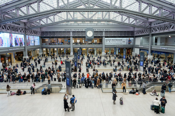 A crowd of people fills a large train hall with a glass roof, seen from an elevated perspective.