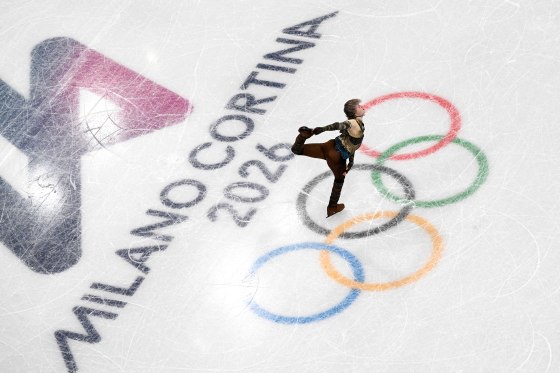 Ilia Malinin holds one heel while skating on a rink with the olympic rings on it.