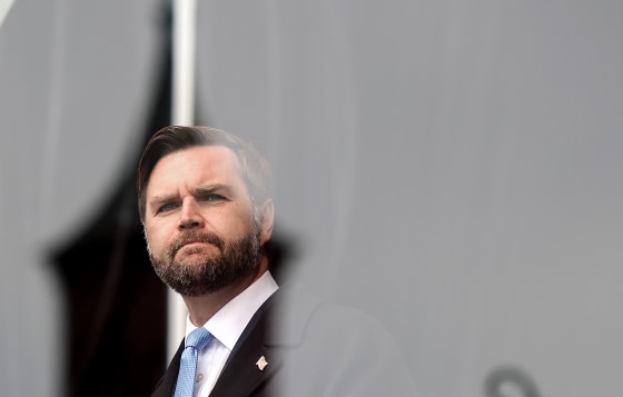 JD Vance appears behind a glass partition while onstage at an outdoor rally.
