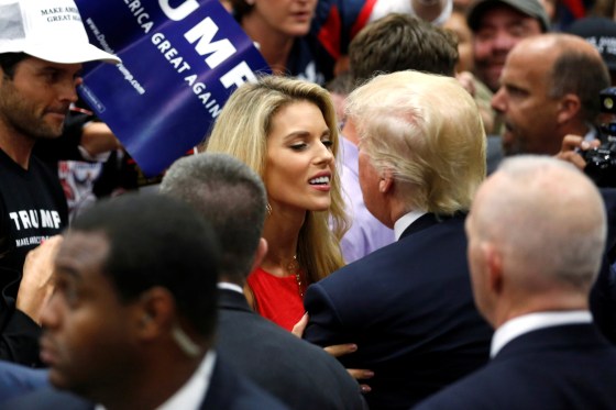 Carie Prejean smiles as she hugs Donald Trump. They are surrounded by a crowd of people