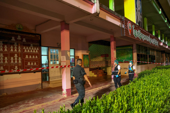 Members of the forensic team and a police officer walk by a school in Thailand, while patrolling a crime scene.