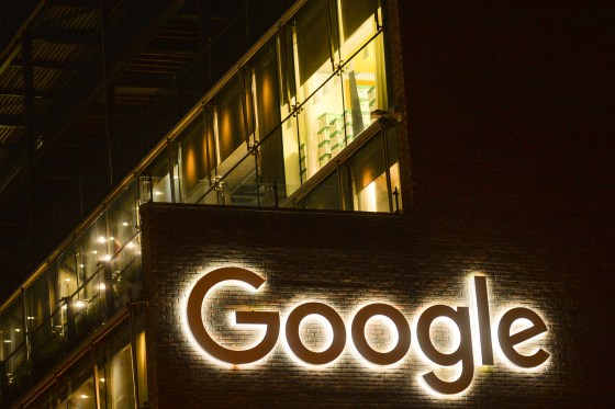 The GOOGLE logo is illuminated on a brick building at night.