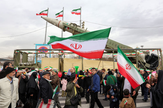 People walk with Iranian national flags near a ballistic missile launch vehicle