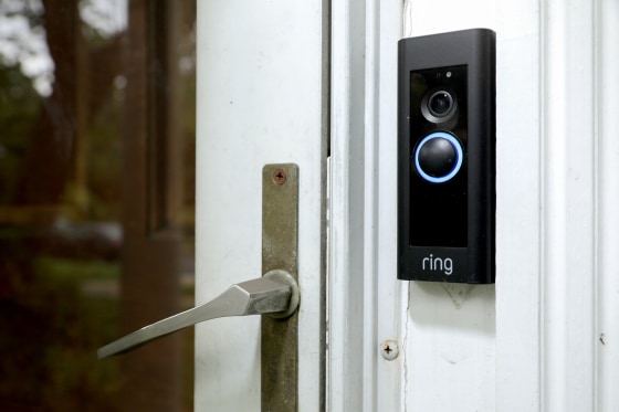 A black Ring doorbell camera is mounted next to the handle of a glass door on the exterior of a house.