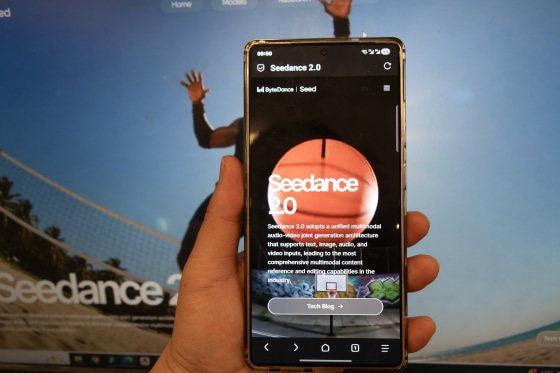A hand holds up a mobile phone in front of a computer screen. Both read "Seedance 2.0".