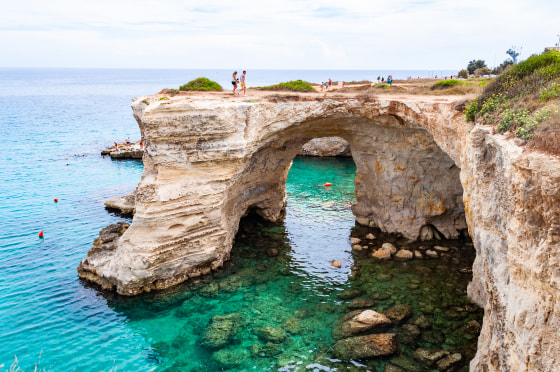 Tourists on the edge of rock. Torre Sant Andrea beach with its soft calcareous rocks and cliffs, sea stacks, small coves and the jagged coast landscape