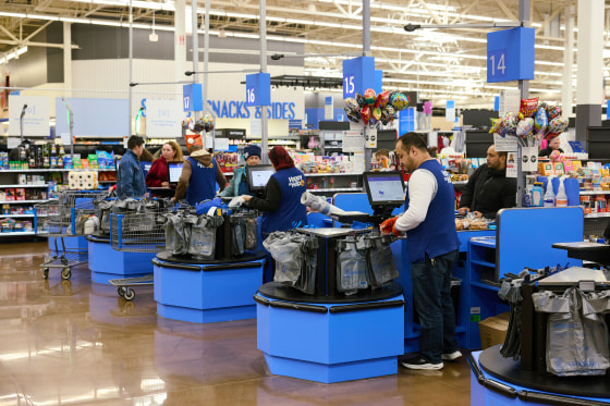 Cashiers and customers are lined up at a series of blue checkout aisles inside a Walmart.