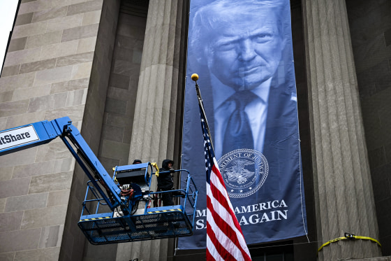 Image: Workers install a new banner featuring an image of President Donald Trump on the facade of the U.S. Department of Justice