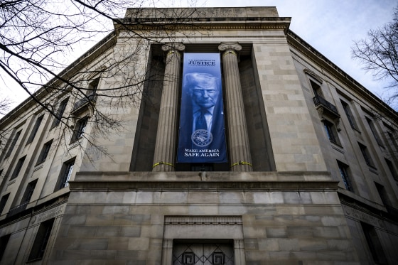 Image: A a new banner featuring an image of President Donald Trump is displayed on the facade of the U.S. Department of Justice 