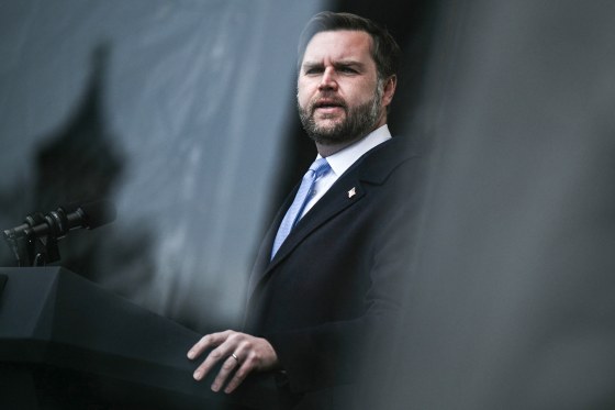 JD Vance speaks at a podium outside behind bulletproof glass
