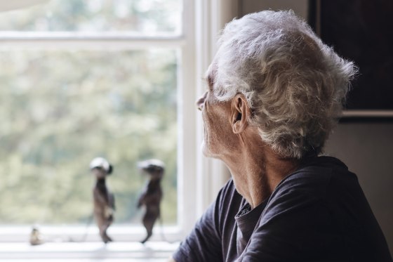 Image: Senior man looking through window while sitting at home
